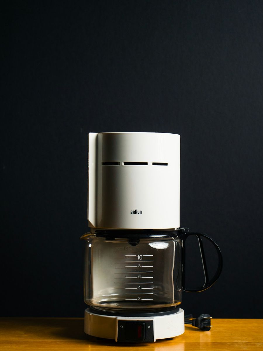 A vintage white Braun drip coffee maker with a 10-cup glass carafe on a wooden table against a dark wall