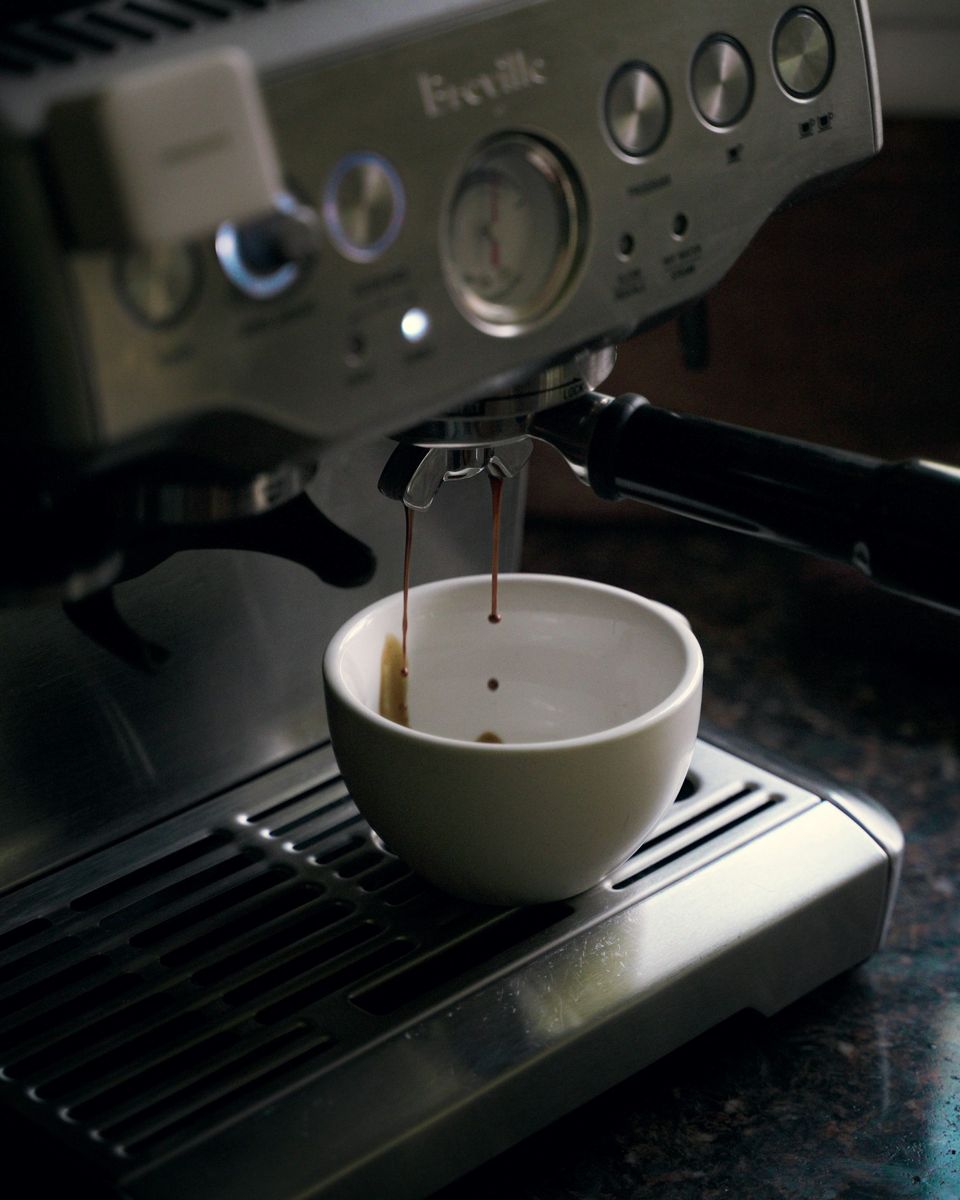 The front panel of a Breville Barista Express with espresso dripping from the portafilter into a white cup