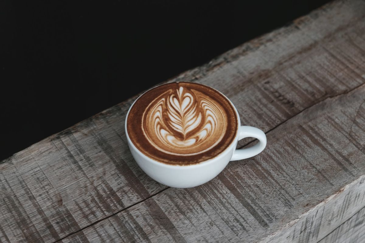 A cappuccino in a small white ceramic cup, with a rosetta poured into a deep layer of foam