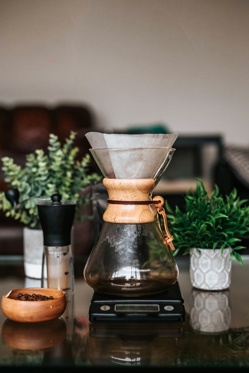 A glass brewer and a hand grinder with coffee beans on a counter