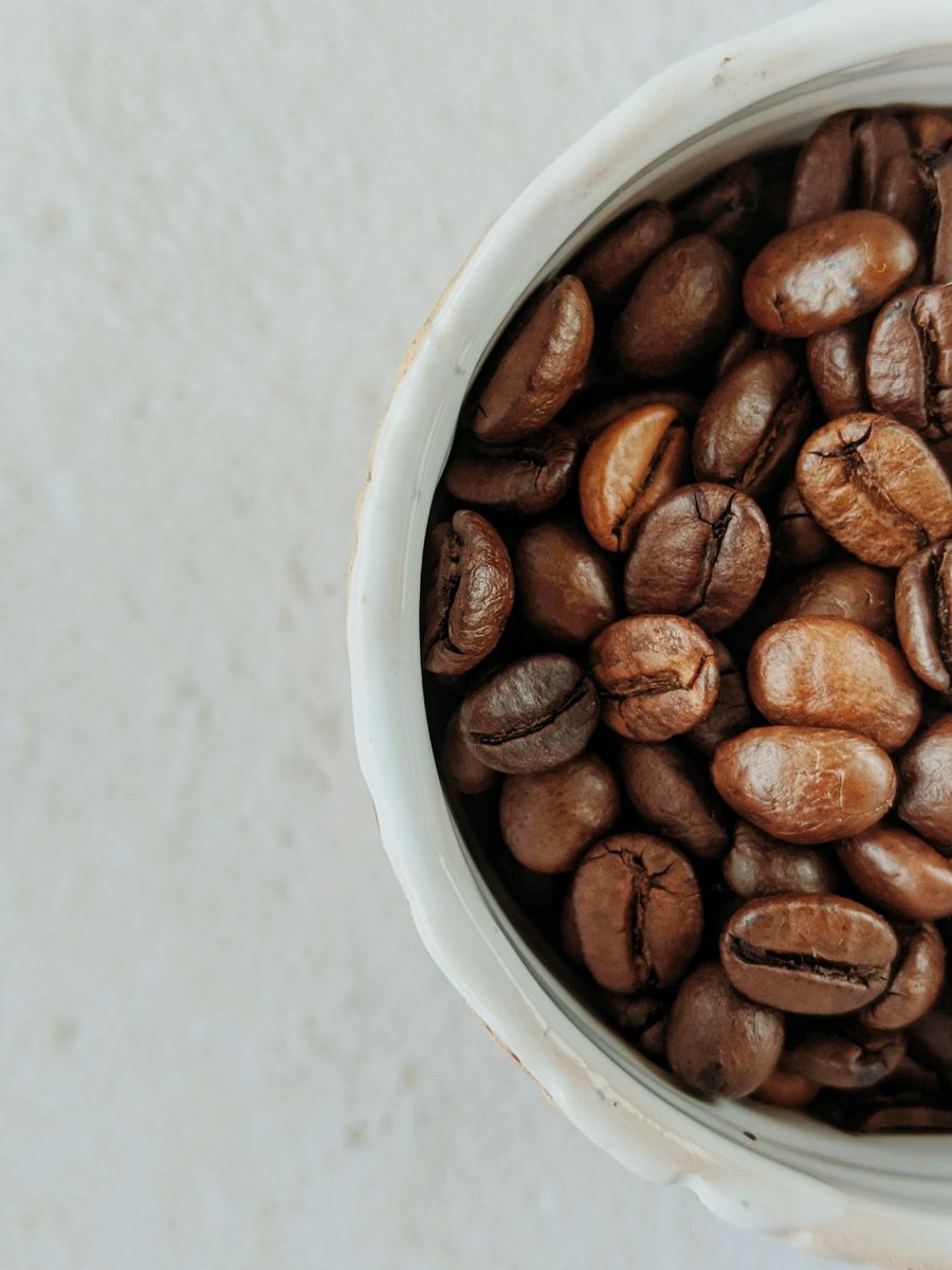 Roasted coffee beans in a white ceramic bowl, lighter and darker beans mixed, with matte surfaces